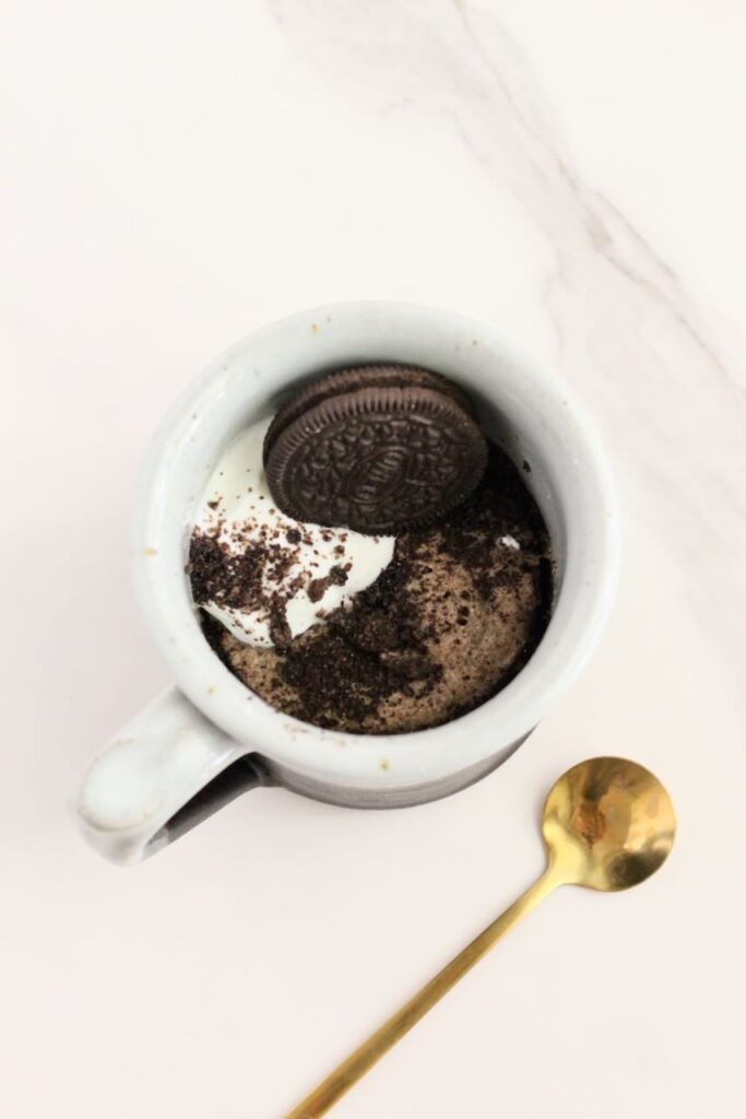 Oreo protein mug cake topped with oreo and gold spoon next to mug