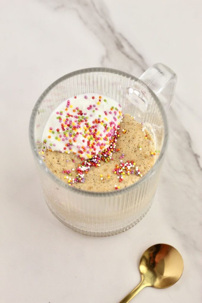 Birthday cake vanilla protein mug cake cooked in clear mug topped with rainbow sprinkles 
