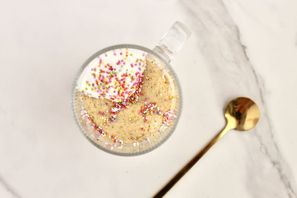 Birthday cake vanilla protein mug cake topped with rainbow sprinkles and gold spoon