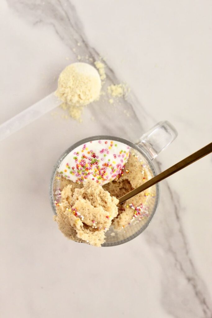 Birthday cake vanilla protein mug cake with spoon in taking scoop out with protein powder in background
