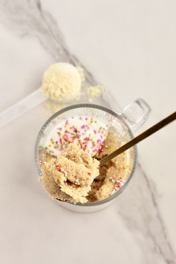 Birthday cake vanilla protein mug cake topped with gold spoon taking scoop out and protein powder in background