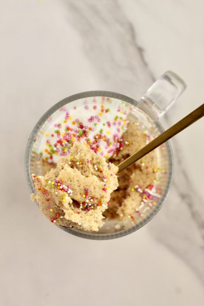 Birthday cake vanilla protein mug cake topped with rainbow sprinkles with scoop being taken out