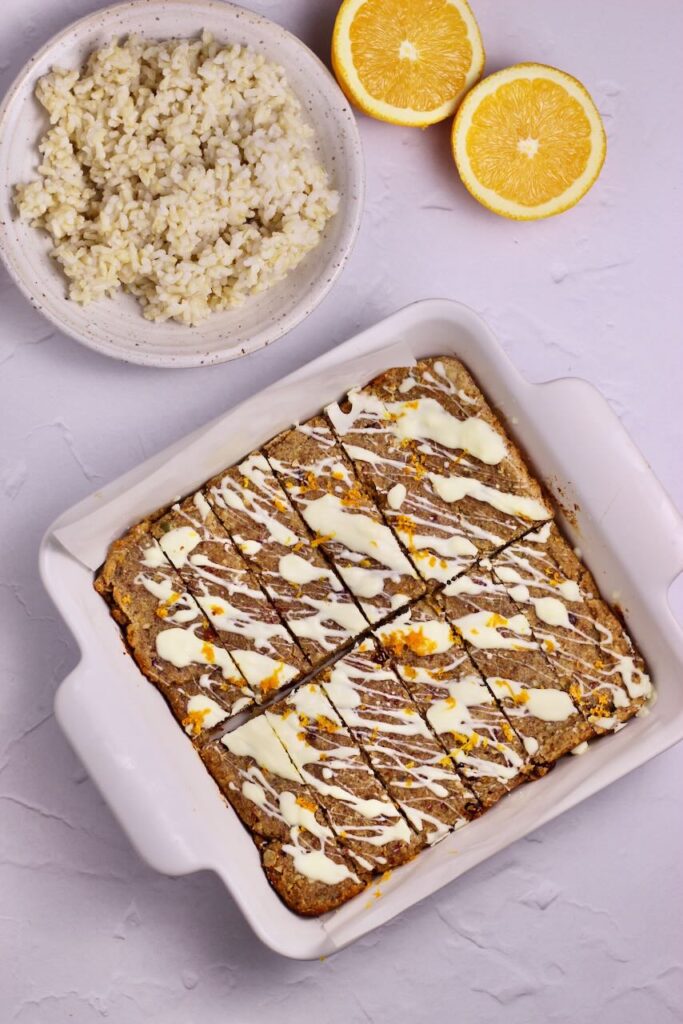 Cranberry Orange Energy Bars in white dish with brown rice on the side with a sliced orange