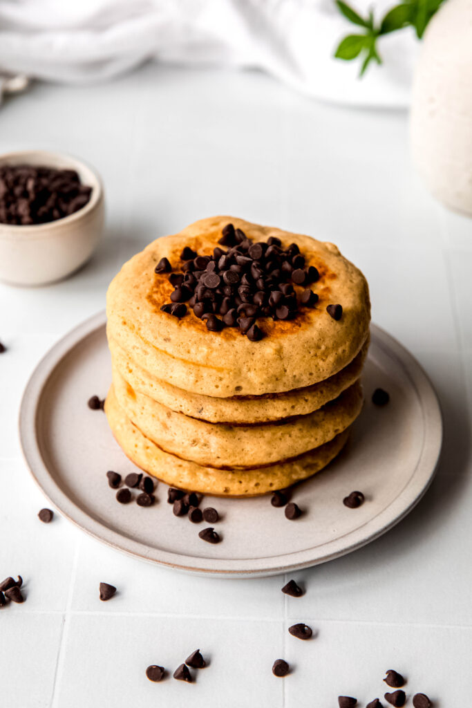 Four protein pancakes stacked topped with chocolate chip on beige plate