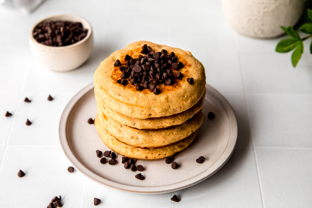 Four protein pancakes stacked topped with chocolate chip on beige plate