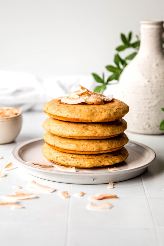 Four protein pancakes stacked  topped with shredded coconut