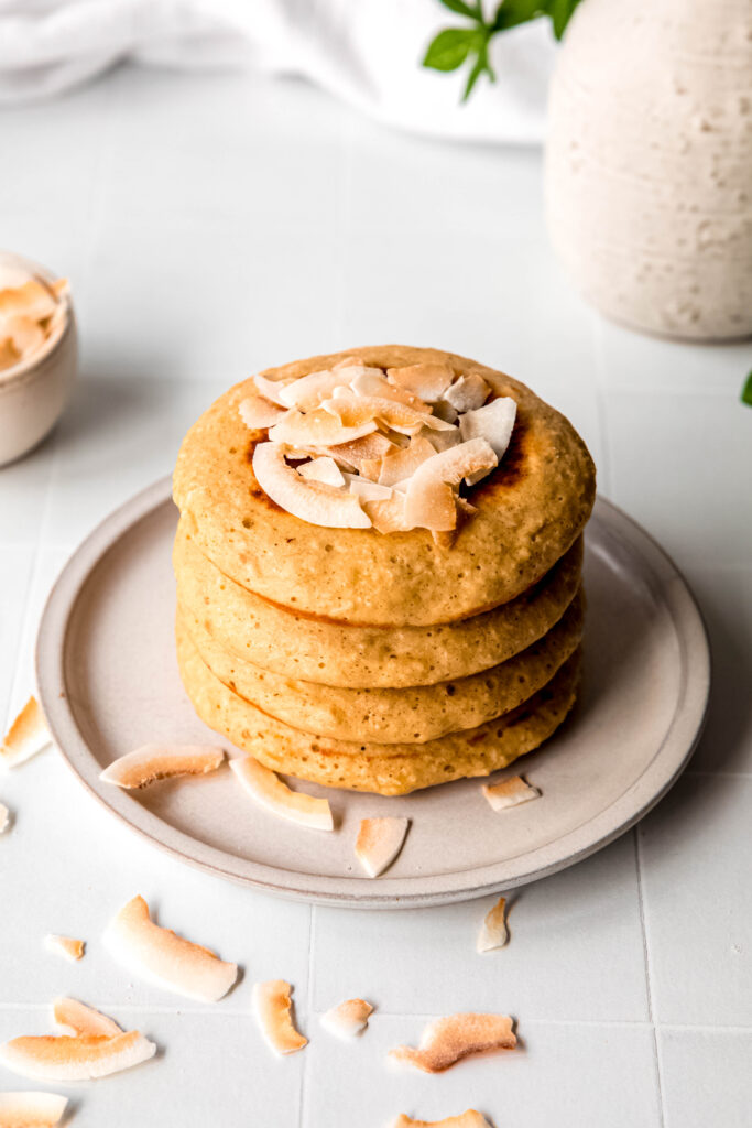 Four protein pancakes stacked topped with shredded coconut