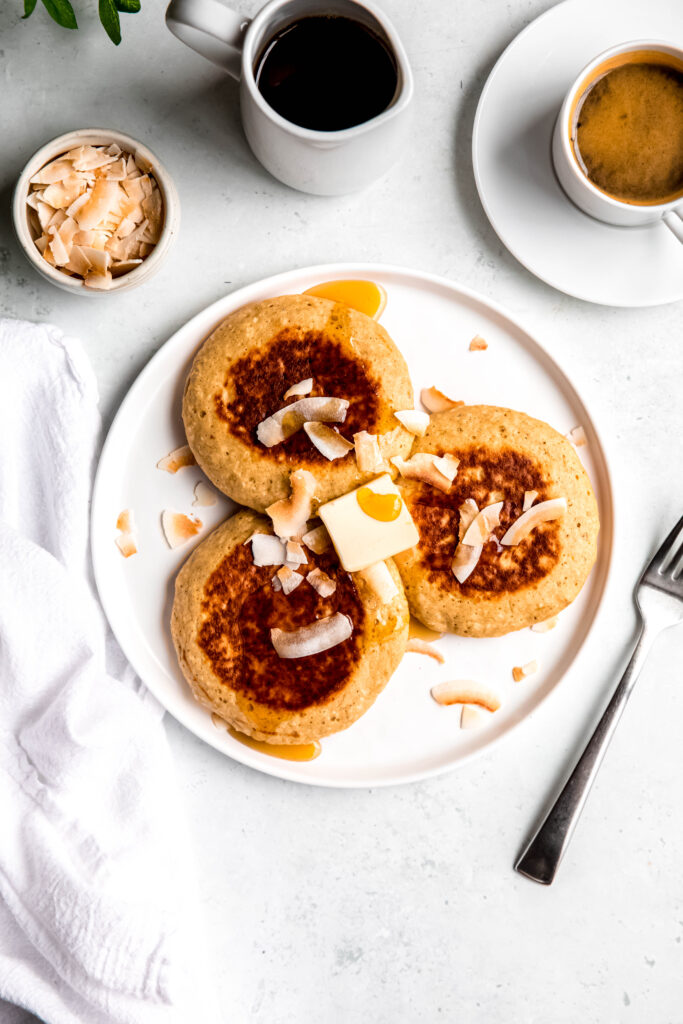 Protein pancakes topped with shredded coconut and syrup on white plate and fork on side