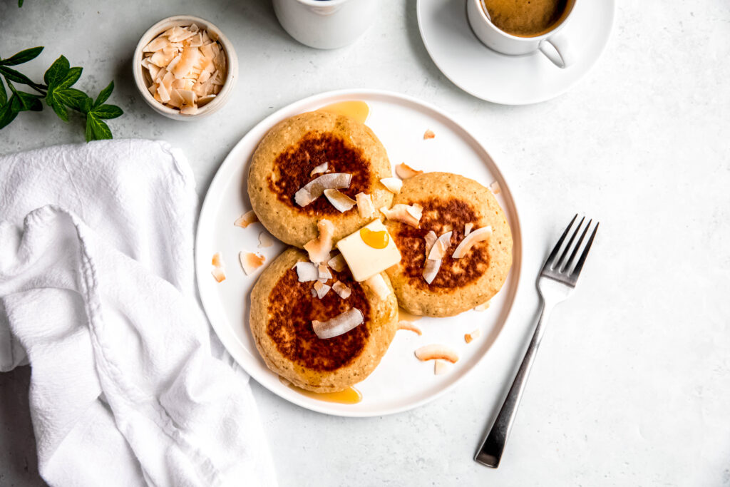 Protein pancakes topped with shredded coconut and syrup on white plate and fork on side