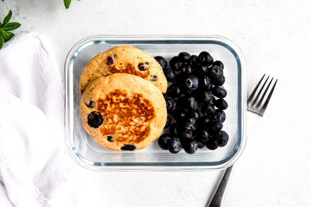 Protein pancakes in meal prep container with blueberries and fork on side