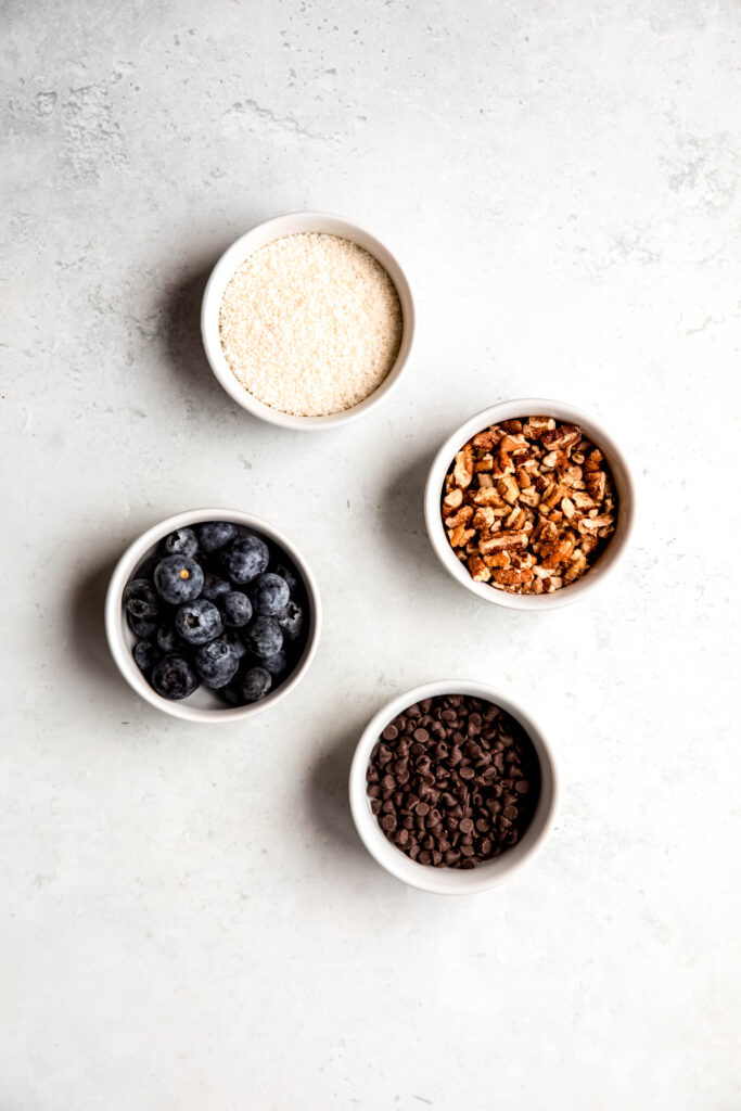 Toppings of your choice: blueberries, pecans, coconut, and chocolate chips in white bowls