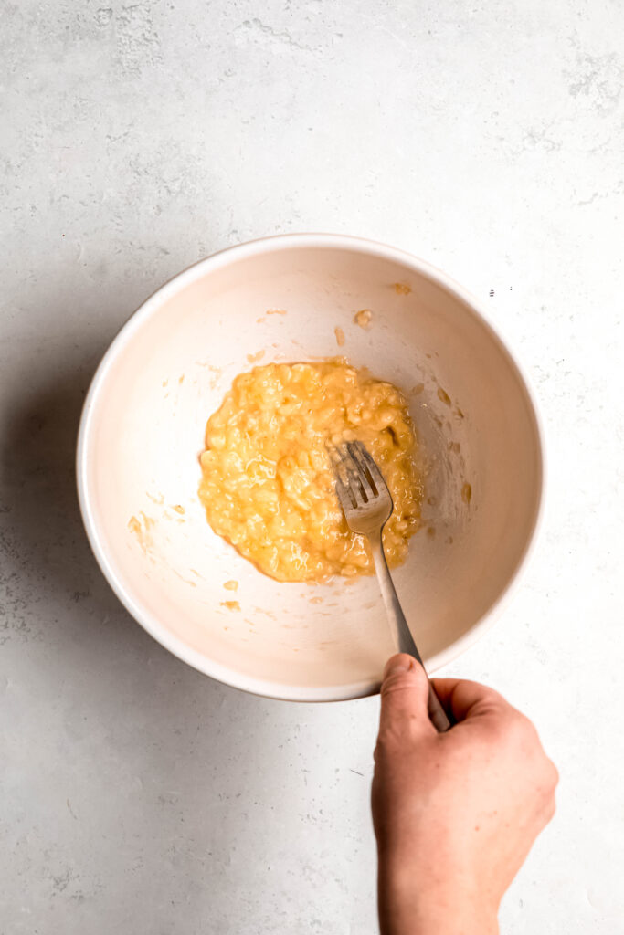 Banana mashed with fork in white bowl