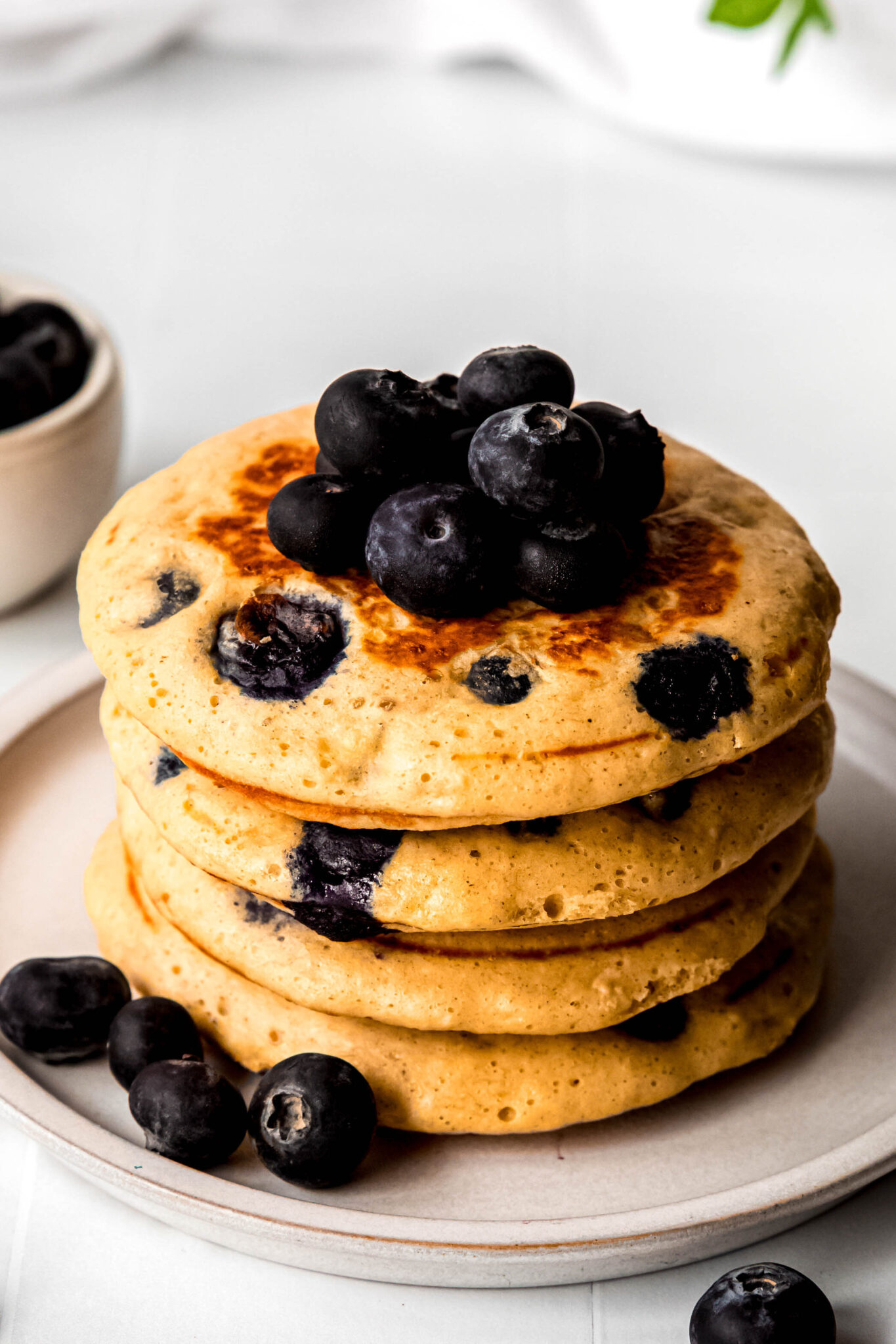 Four protein pancakes stacked topped with blueberries on beige plate