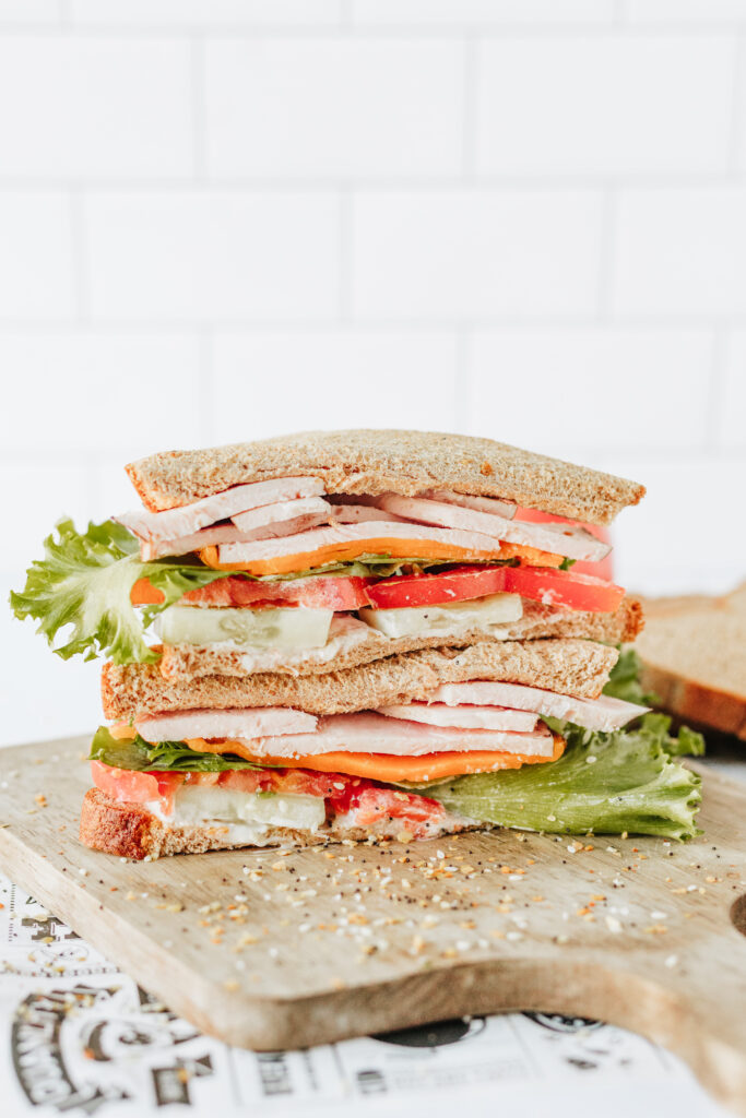 Customizable healthy sandwich showing layers of veggies, protein, cheese, and bread on wood cutting board