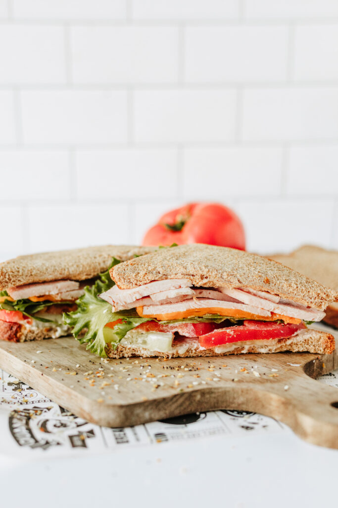 Customizable healthy sandwich showing layers of veggies, protein, cheese, and bread on cutting board