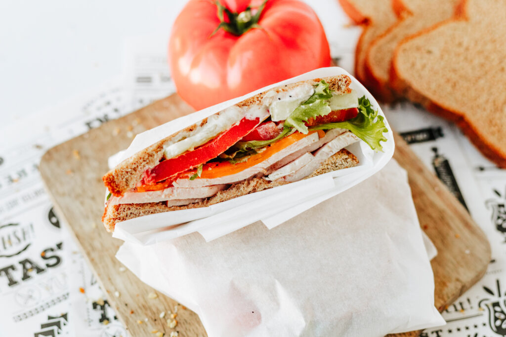 Customizable healthy sandwich cut in half showing layers with tomato in background