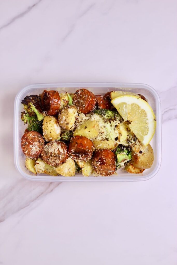 Sheet pan sausage and veggies in meal prep container and fresh lemon slice