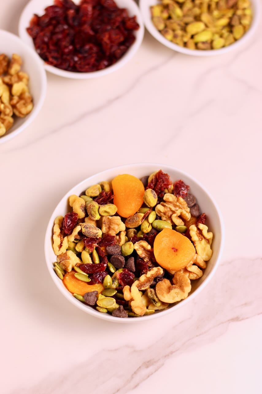 Homemade Trail Mix Recipe in white bowl with ingredients of your choice in background