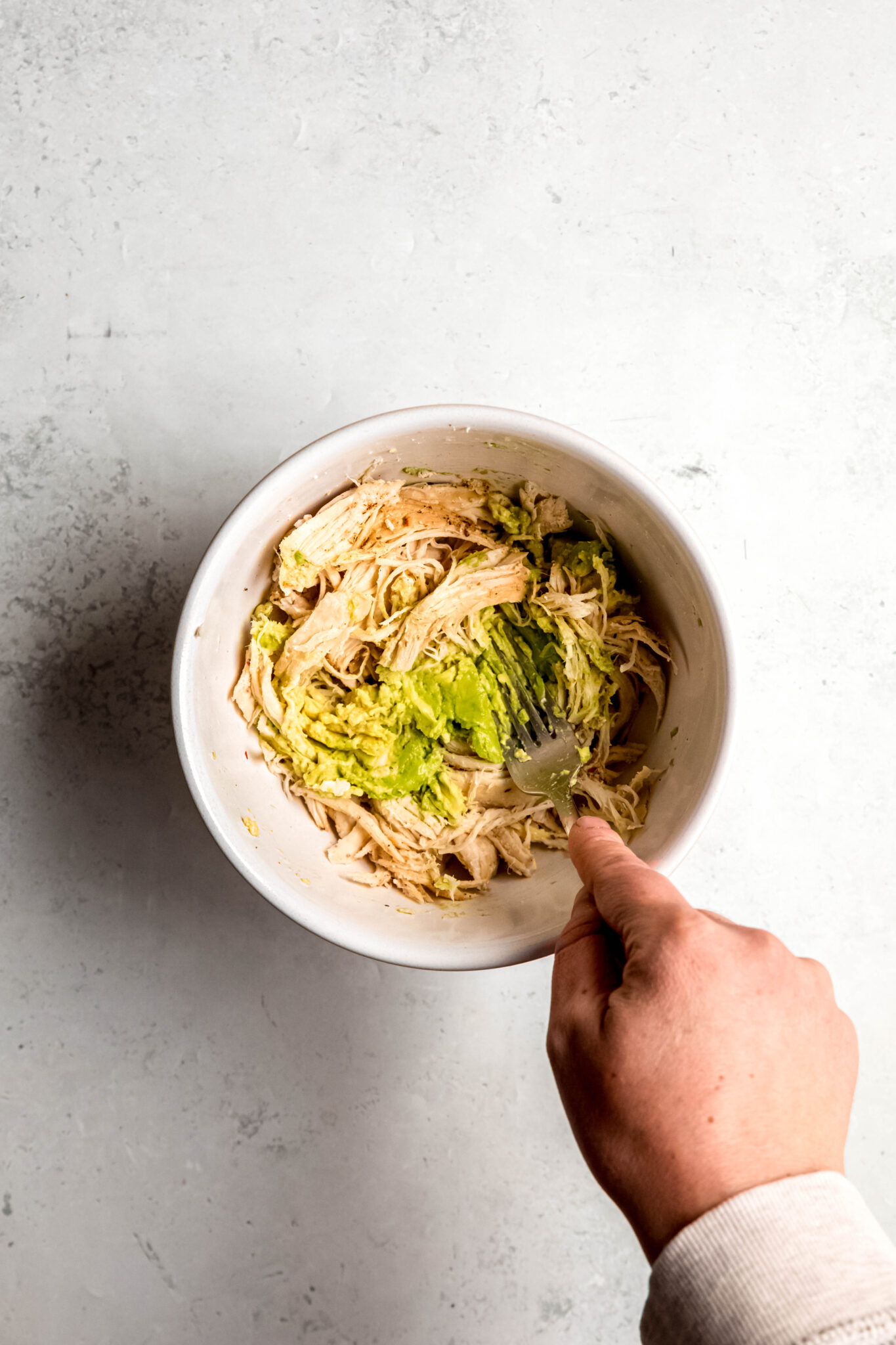 Mashing avocado and chicken in white bowl