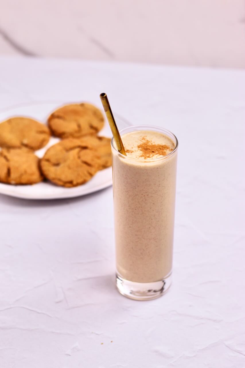 Gingerbread protein smoothie in glass with straw with cookies in the background
